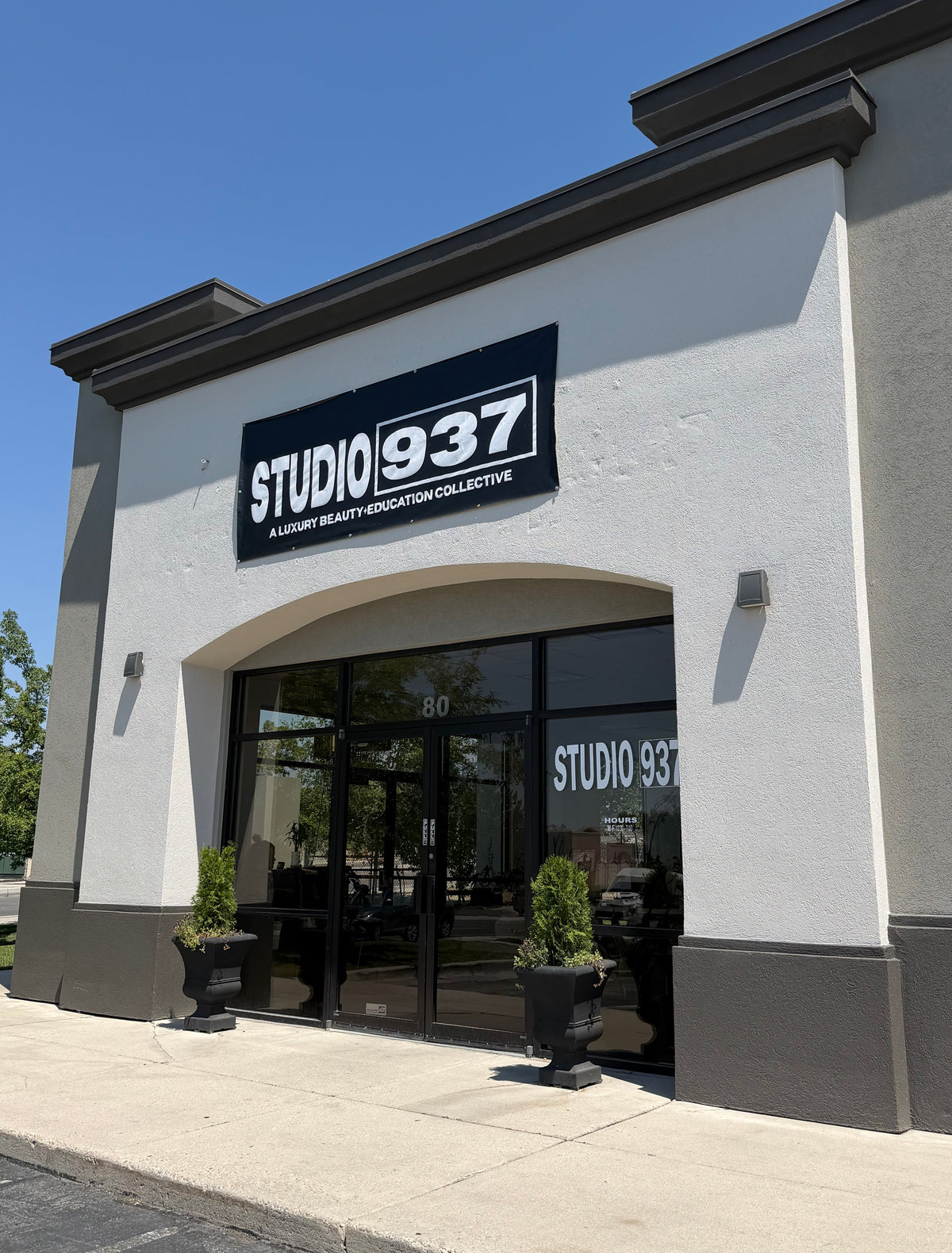 Studio 937 storefront exterior with a black sign above glass doors, set against a white and gray building facade under a clear blue sky.
